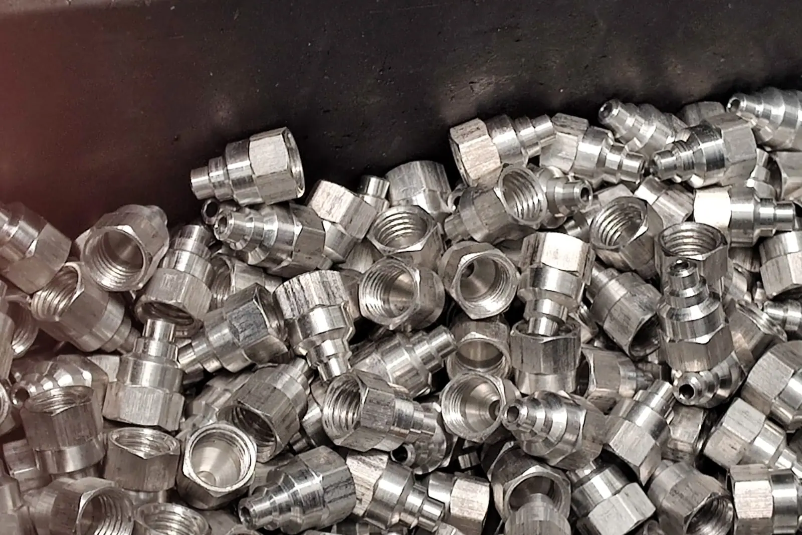 Conexões de metal usinadas, brilhando, amontoadas numa caixa